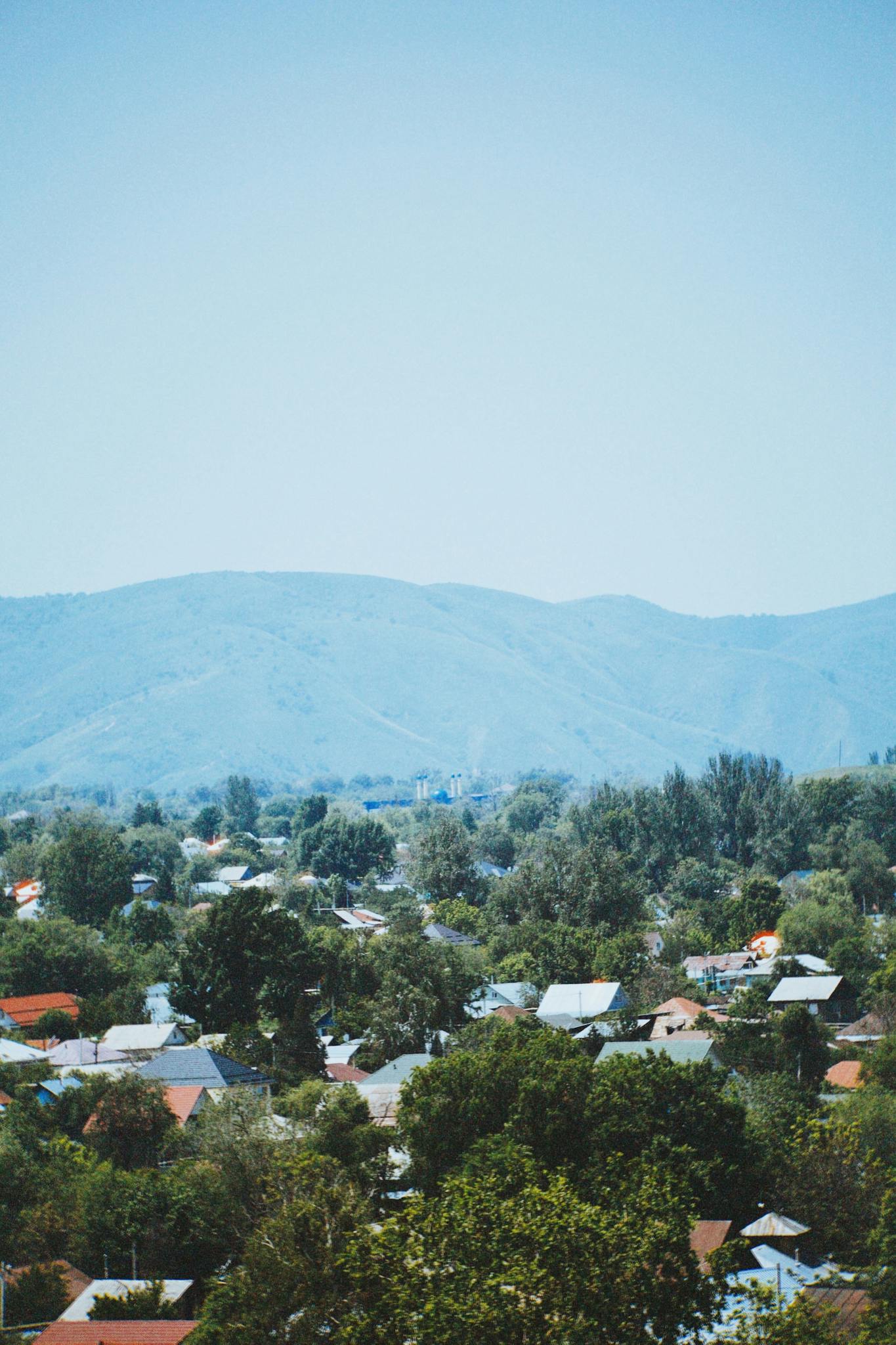 A picturesque view of houses nestled among trees with the mountains of Talgar, Kazakhstan in the background.