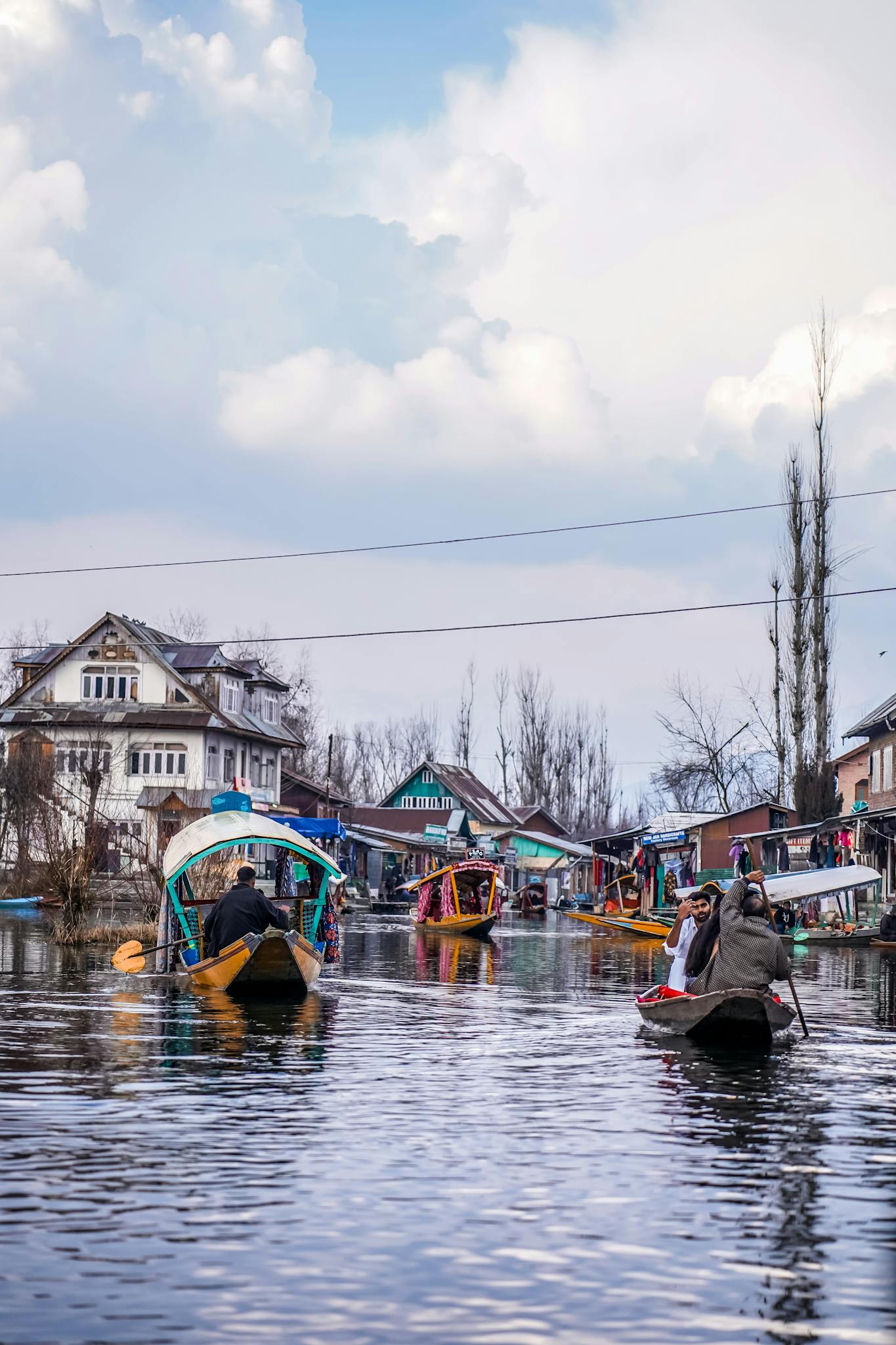 Colorful boats navigate a scenic canal, lined with picturesque houses under a partly cloudy sky.