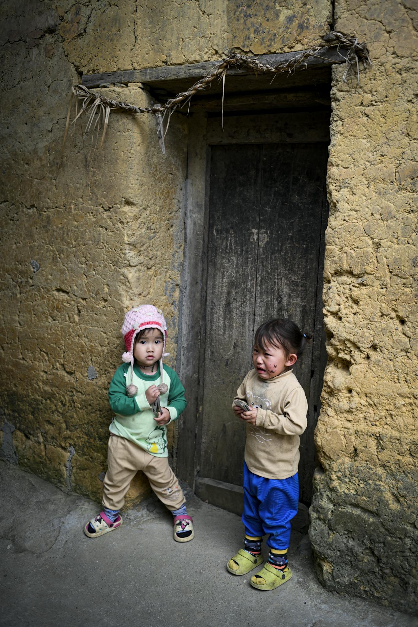 Two children in Hà Giang, Vietnam, against rustic wall.